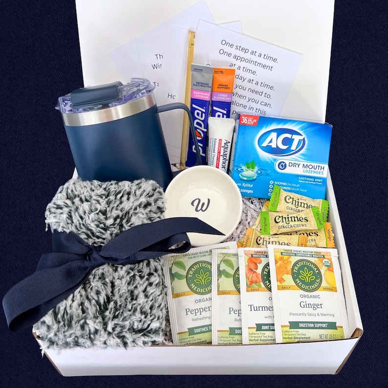 Peut inclure: Un coffret cadeau rempli d'articles de soins personnels. Il comprend un gobelet bleu marine, un petit bol blanc avec un "W", une &eacute;charpe grise duveteuse avec un n&oelig;ud bleu marine, des sachets de th&eacute;, des pastilles, un baume &agrave; l&egrave;vres et des sachets d'&eacute;lectrolytes. La bo&icirc;te contient une note.