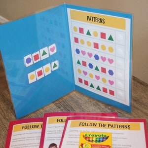 May include: A blue folder with pattern matching activities. The folder displays a chart with colorful shapes and a matching activity. Several cards with the text "Follow the Patterns" are visible, along with a box of crayons.