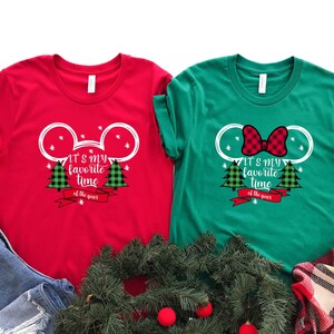 Puede incluir: Dos camisetas de Navidad rojas y verdes con un dise&ntilde;o de cabeza de Mickey Mouse. El texto en las camisetas dice "It's my favorite time of the year".