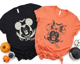 May include: A black t-shirt featuring a distressed white graphic of Mickey Mouse as a vampire with bats, and an orange t-shirt featuring a distressed black graphic of Minnie Mouse with a bow and bats. Both shirts include small decorative pumpkins.