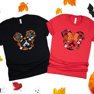 May include: Two black and red t-shirts with a Halloween-themed Mickey Mouse and Minnie Mouse design. The Mickey Mouse design features a black silhouette of Mickey's head with a castle, bats, pumpkins, and spiderwebs. The Minnie Mouse design features a red bow with white polka dots and a castle, bats, pumpkins, and spiderwebs.
