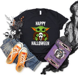 K&ouml;nnte beinhalten: Schwarzes T-Shirt mit einer gr&uuml;nen und braunen Comicfigur, die eine wei&szlig;e Geistermaske h&auml;lt. Der Text "Happy Halloween" ist unter der Figur gedruckt.