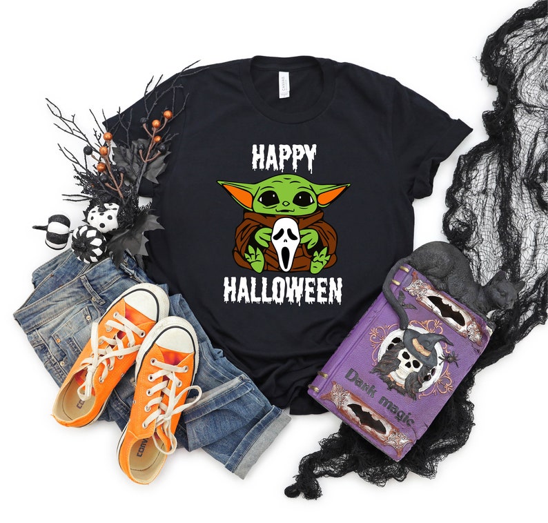 K&ouml;nnte beinhalten: Schwarzes T-Shirt mit einer gr&uuml;nen und braunen Comicfigur, die eine wei&szlig;e Geistermaske h&auml;lt. Der Text "Happy Halloween" ist unter der Figur gedruckt.