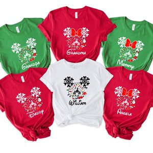 May include: Six red and green t-shirts with a white Mickey Mouse head design featuring a Christmas tree, lights, and ornaments. The shirts have the words "Grandma", "Grandpa", "Mommy", "Daddy", "William", and "Angela" printed on them.