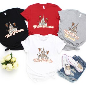 May include: Five t-shirts with a graphic of Cinderella's castle and text that reads "The Groom", "Bridemaid", "Maid of Honor", and "The Bride".