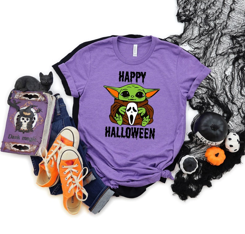 K&ouml;nnte beinhalten: Lilafarbenes T-Shirt mit einer gr&uuml;nen Alienfigur, die eine wei&szlig;e Geistermaske h&auml;lt. Auf dem Shirt steht "Happy Halloween".