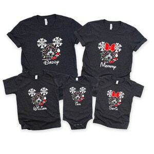 May include: A set of five gray t-shirts featuring a Mickey Mouse silhouette with Christmas lights, ornaments, and snowflakes. The shirts are personalized with the names "Daddy", "Mommy", "William", "Tom", and "Sofia".