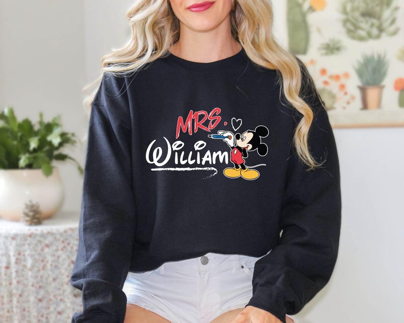 May include: Black sweatshirt with the text "MRS. (William)" in white with a red heart and a cartoon Mickey Mouse holding a pencil.