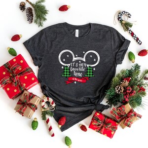 Puede incluir: Una camiseta gris oscuro con una silueta blanca de Mickey Mouse y dos &aacute;rboles de Navidad de cuadros verdes y rojos. El texto "It's my favorite time of the year" est&aacute; impreso en la camiseta.