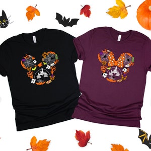 May include: Two t-shirts with a Halloween Mickey Mouse design. The black shirt has a white Mickey Mouse head with a spiderweb, castle, and other Halloween elements. The maroon shirt has a white Mickey Mouse head with a bow, spiderweb, castle, and other Halloween elements.
