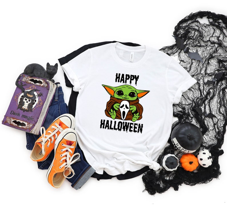 K&ouml;nnte beinhalten: Wei&szlig;es T-Shirt mit einer gr&uuml;nen Baby-Yoda-Figur, die eine wei&szlig;e Geistermaske h&auml;lt. Der Text "HAPPY HALLOWEEN" ist in Schwarz unter der Figur gedruckt.