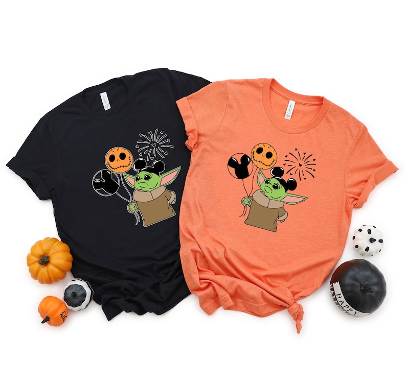 Pu&ograve; includere: Due t-shirt con un personaggio alieno verde che tiene palloncini arancioni e neri con orecchie di Topolino. L'alieno indossa una camicia marrone. Le t-shirt sono nere e arancioni.