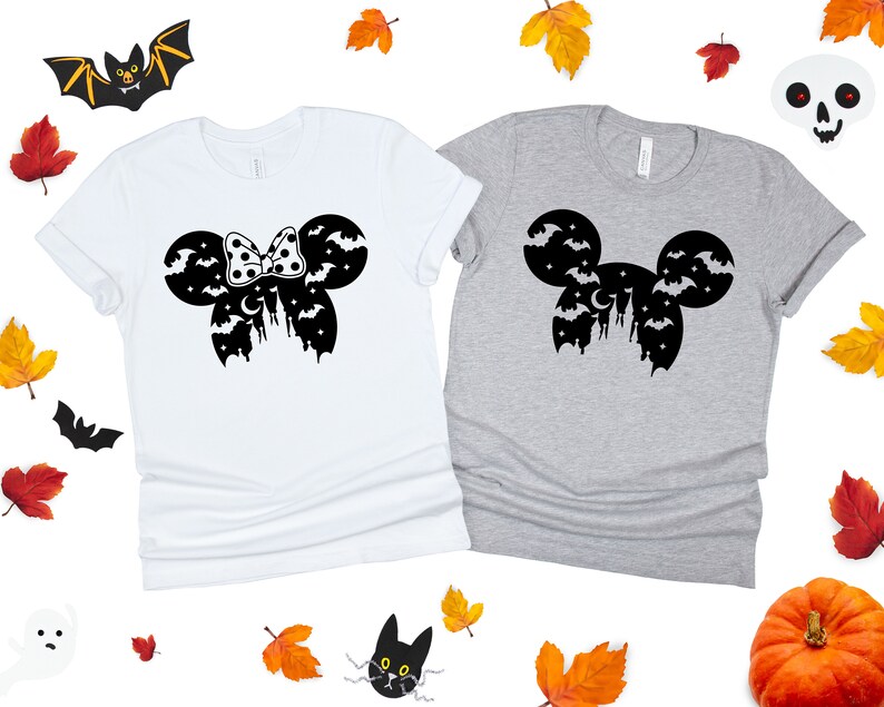 May include: Two t-shirts with a Halloween-themed Mickey Mouse design. One shirt is white with a black bow and the other is gray with a black Mickey Mouse head.