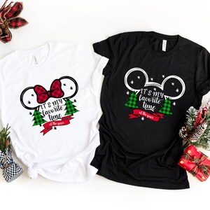 Puede incluir: Dos camisetas con tem&aacute;tica navide&ntilde;a. Una es blanca con un lazo rojo y la otra es negra con orejas de Mickey Mouse. Ambas camisetas tienen &aacute;rboles de Navidad de cuadros verdes y rojos y el texto "Es mi &eacute;poca favorita del a&ntilde;o."