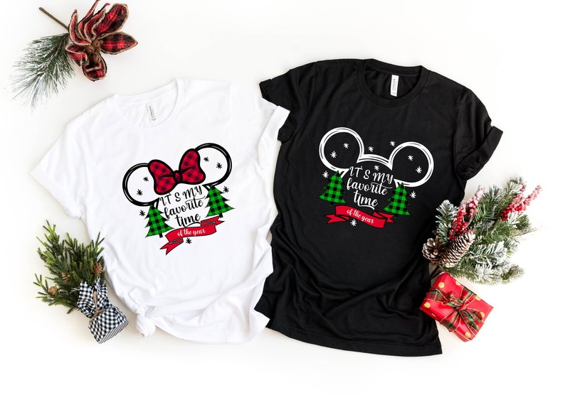 Puede incluir: Dos camisetas con tem&aacute;tica navide&ntilde;a. Una es blanca con un lazo rojo y la otra es negra con orejas de Mickey Mouse. Ambas camisetas tienen &aacute;rboles de Navidad de cuadros verdes y rojos y el texto "Es mi &eacute;poca favorita del a&ntilde;o."