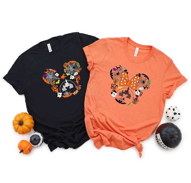 May include: Two t-shirts with a Halloween Mickey Mouse design. The black t-shirt has a Mickey Mouse head made of Halloween icons, including a castle, ghosts, pumpkins, and bats. The orange t-shirt has a Minnie Mouse head made of Halloween icons, including a bow, a castle, ghosts, pumpkins, and bats.