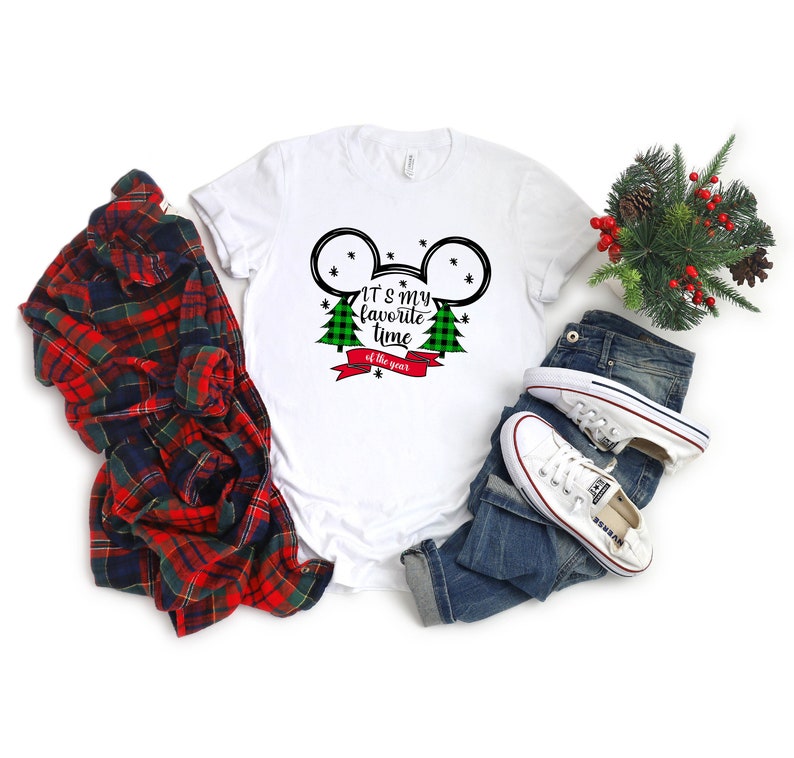 Puede incluir: Camiseta blanca con una silueta de Mickey Mouse en blanco y negro con &aacute;rboles de Navidad de cuadros verdes y negros y una cinta roja con el texto "Es mi &eacute;poca favorita del a&ntilde;o".