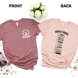 May include: Two t-shirts, one in a dusty rose color and the other in a light peach color. The dusty rose shirt has a white graphic on the front that says "Ever After" with a crown and a small graphic of a dog. The peach shirt has a black graphic on the back that says "World Crawl" with a checklist of countries.