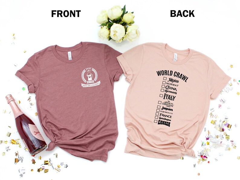 May include: Two t-shirts, one in a dusty rose color and the other in a light peach color. The dusty rose shirt has a white graphic on the front that says "Ever After" with a crown and a small graphic of a dog. The peach shirt has a black graphic on the back that says "World Crawl" with a checklist of countries.
