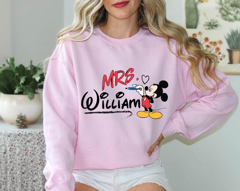 May include: Pink sweatshirt with a Mickey Mouse graphic and the text "MRS. WILLIAM" in black.