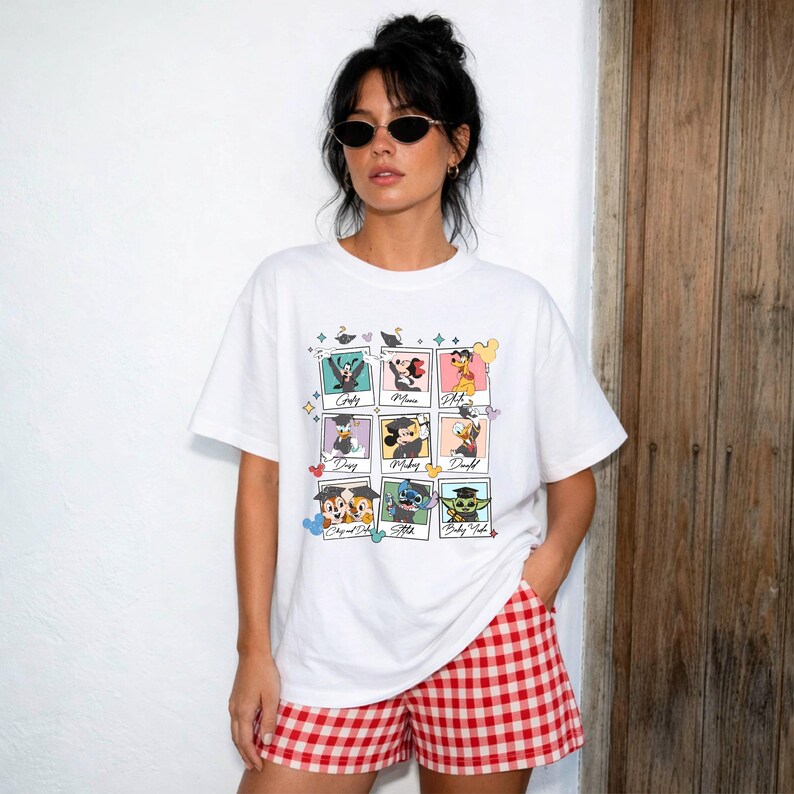 May include: White t-shirt featuring a collage of Disney characters in graduation caps. The characters include Goofy, Minnie Mouse, Donald Duck, Chip and Dale, Stitch, and Baby Yoda. The model is wearing red and white checkered shorts.