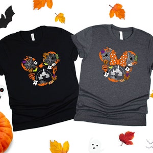 May include: Two black and gray t-shirts with a Halloween Mickey Mouse and Minnie Mouse design. The Mickey Mouse design features a black and orange castle with bats, ghosts, and pumpkins. The Minnie Mouse design features a red and white polka dot bow with bats, ghosts, and pumpkins.