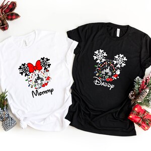May include: Two white and black t-shirts with a Christmas Mickey Mouse design. The white shirt says "Mommy" and the black shirt says "Daddy".