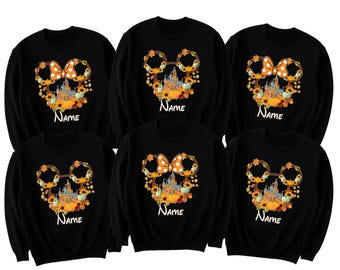 Puede incluir: Sudaderas negras con un diseño en forma de Mickey Mouse. El diseño incluye un lazo, hojas de otoño, un castillo y la palabra "Name" en blanco. El diseño incorpora colores naranja, amarillo y verde, perfecto para el otoño o eventos temáticos de Disney.