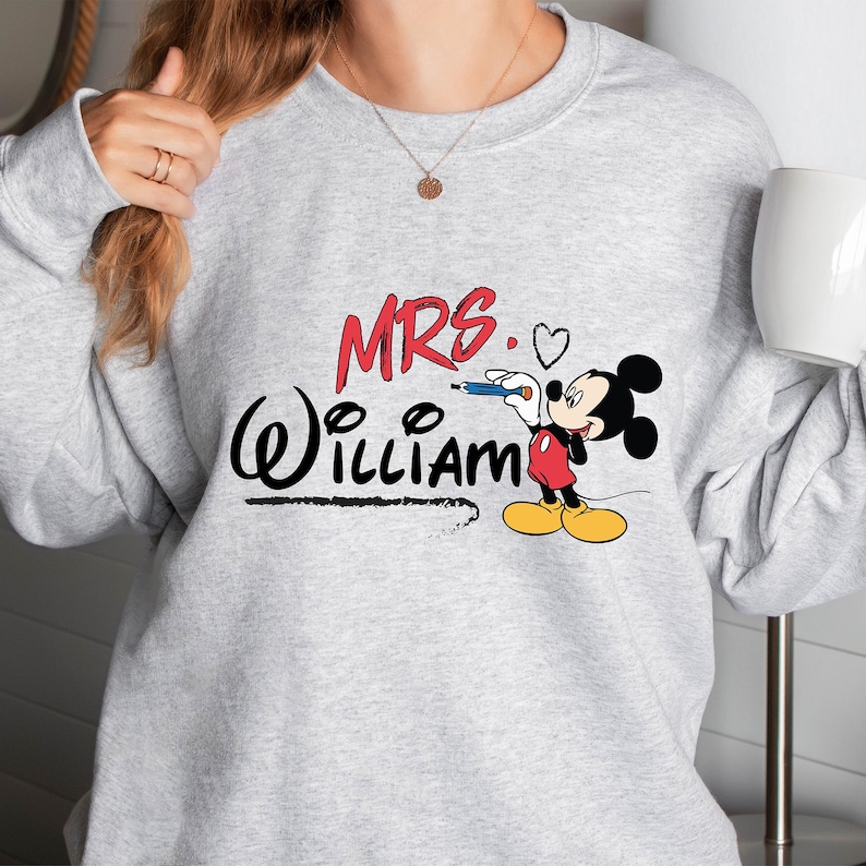 May include: Gray sweatshirt with a red and black Mickey Mouse design. The text "MRS. William" is written in black with a heart next to the word "MRS."