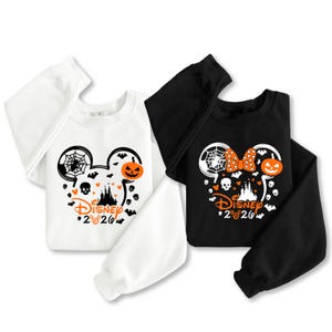 May include: A white sweatshirt and a black sweatshirt, each featuring a graphic of Mickey Mouse ears filled with Halloween motifs including a spider web, a jack-o'-lantern, bats, skulls, and a castle, with the text Disney 2026 printed below.