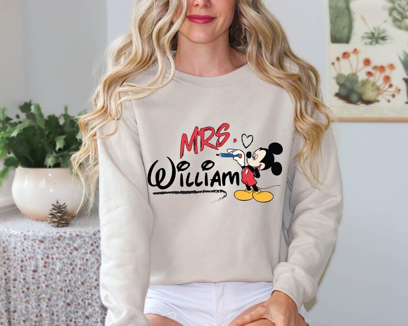 May include: A beige sweatshirt with a Mickey Mouse graphic and the text "MRS. William" in black and red.