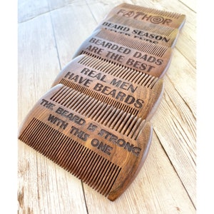 May include: Set of five wooden beard combs with different engraved sayings. The sayings are "FATHOR", "BEARD SEASON", "BEARDED DADS ARE THE BEST", "REAL MEN HAVE BEARDS", and "THE BEARD IS STRONG WITH THIS ONE".