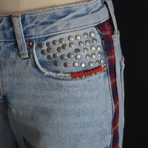 K&ouml;nnte beinhalten: Hellblaue Jeans mit silbernen Nieten auf der Vordertasche. Mit roter, gen&auml;hter Taschenverkleidung und einem rot-blau-braunen Karostreifen an der Seite. Abgenutzte Details sorgen f&uuml;r einen Vintage-Look.