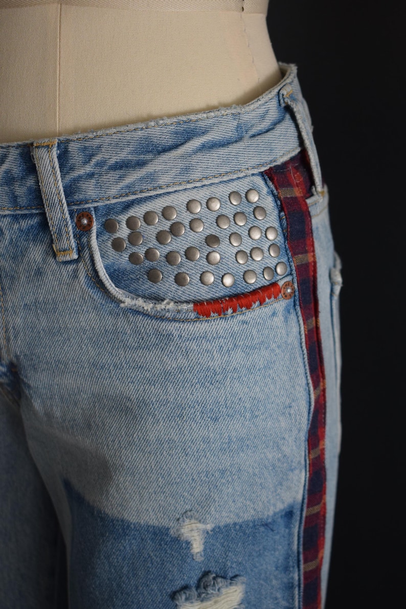 K&ouml;nnte beinhalten: Hellblaue Jeans mit silbernen Nieten auf der Vordertasche. Mit roter, gen&auml;hter Taschenverkleidung und einem rot-blau-braunen Karostreifen an der Seite. Abgenutzte Details sorgen f&uuml;r einen Vintage-Look.