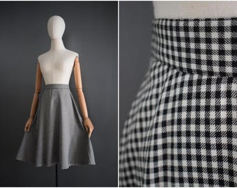 May include: A black and white checkered skirt displayed on a mannequin. The skirt has a high waist and a flared A-line shape. The fabric is a classic gingham pattern, and the skirt is knee-length.