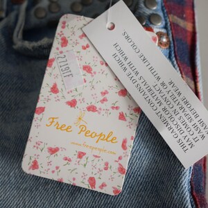 K&ouml;nnte beinhalten: Nahaufnahme einer Jeans aus Denim mit einem floralen Etikett von Free People. Das Etikett hat rosa Rosen auf wei&szlig;em Grund und den Text "Free People". Ein zweites Etikett enth&auml;lt Waschanweisungen.
