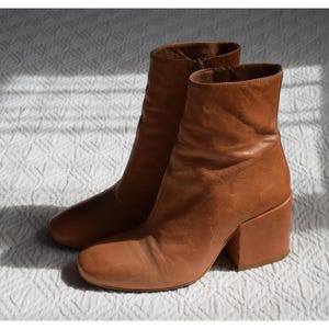 Peut inclure: Une paire de bottines en cuir marron à talons blocs. Les bottines ont une pointe pointue et une fermeture éclair à l'intérieur de la cheville.