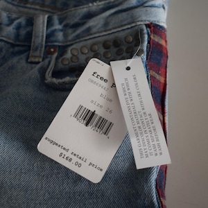 K&ouml;nnte beinhalten: Hellblaue Jeans mit einem rot-blau karierten Seitenakzent. Die Jeans hat Metallnieten und ein Etikett mit "free people" und Gr&ouml;&szlig;e 26. Der empfohlene Verkaufspreis betr&auml;gt 168,00 $.