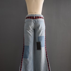 K&ouml;nnte beinhalten: Hellblaue Jeanshose mit weitem Bein. Die Hose hat rot-schwarze Karomuster an den Seiten und einen Karog&uuml;rtel. Auf der Vorderseite der Hose sind blaue Jeans-Patches und ein schwarzer Patch aufgen&auml;ht.