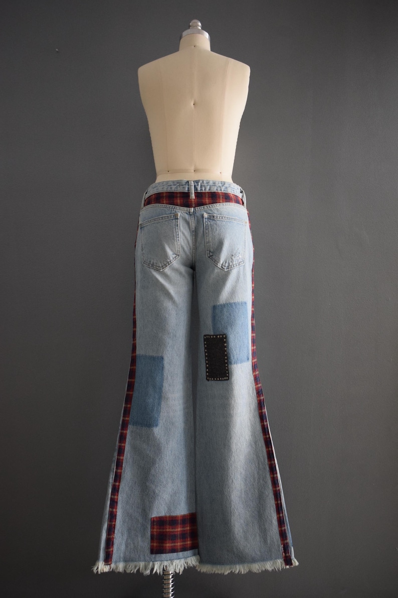 K&ouml;nnte beinhalten: Hellblaue Jeanshose mit weitem Bein. Die Hose hat rot-schwarze Karomuster an den Seiten und einen Karog&uuml;rtel. Auf der Vorderseite der Hose sind blaue Jeans-Patches und ein schwarzer Patch aufgen&auml;ht.