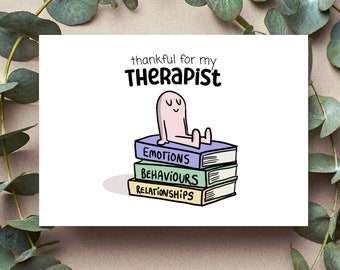 May include: A card with a cartoon illustration of a person sitting on top of a stack of books labeled "Emotions", "Behaviours", and "Relationships". The text "thankful for my therapist" is above the illustration.