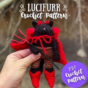 May include: A handmade crochet devil cat doll with a red cape, boots, and trident. The doll is black, brown, and red, with the text "LUCIFURR Crochet Pattern" and "PDF Crochet pattern". The doll is held in a person's hand.