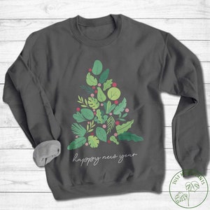 May include: Charcoal grey sweatshirt featuring a Christmas tree design made of green leaves and pink berries. The words "happy new year" are written in a cursive script across the bottom.