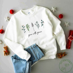 May include: White sweatshirt with a green and red floral design and the text "grow with grace".