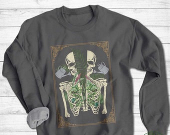 May include: A dark gray sweatshirt with a graphic print of two skeletons with plants growing out of their ribcages. The skeletons are holding watering cans. The graphic is framed in a gold ornate frame.