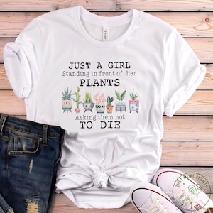 May include: White t-shirt with a graphic of potted plants and the text "Just a girl standing in front of her plants asking them not to die."