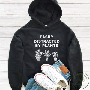 May include: Black hoodie with the text "Easily Distracted By Plants" and a graphic of three potted plants.