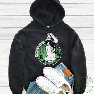 May include: Black hoodie with a green circle graphic featuring a woman watering plants. The text "Bloom with Grace" is written around the circle. The text "Love" is written below the circle.