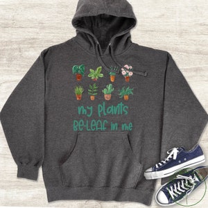 May include: A dark grey hoodie with a graphic of potted plants and the text "my plants be-leaf in me".