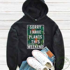 May include: Black hoodie with a white graphic that says "Sorry I have plants this weekend" surrounded by green and red tropical leaves.